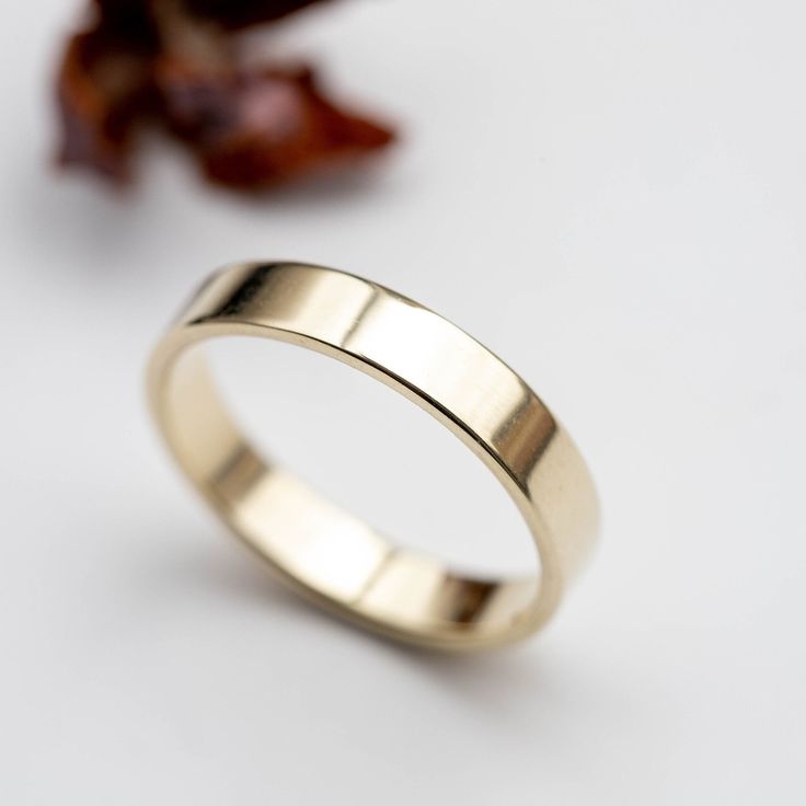 a gold wedding ring sitting on top of a white table next to a dried flower