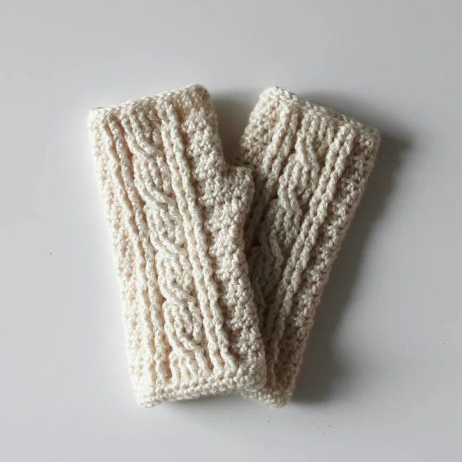 two white knitted mittens sitting on top of a white table next to each other