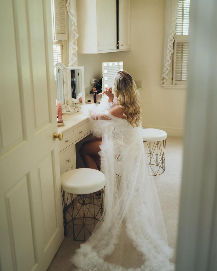 a woman sitting at a vanity in front of a mirror wearing a white wedding dress