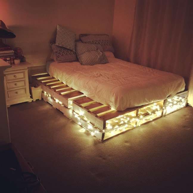 a bed made out of pallets with lights on the bottom and sides, in a bedroom