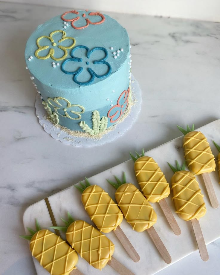 there are pineapples on skewers next to a blue and yellow cake