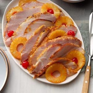 a white plate topped with ham and pineapple slices next to silverware on a table