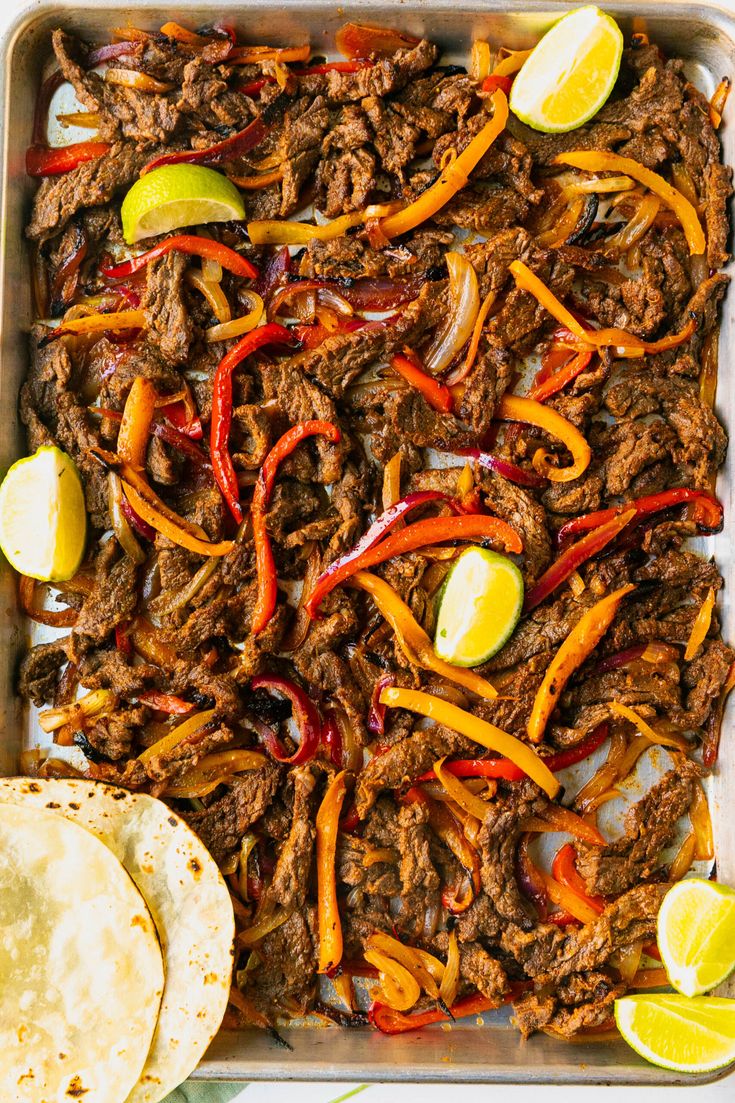 a tray filled with meat, peppers and tortillas