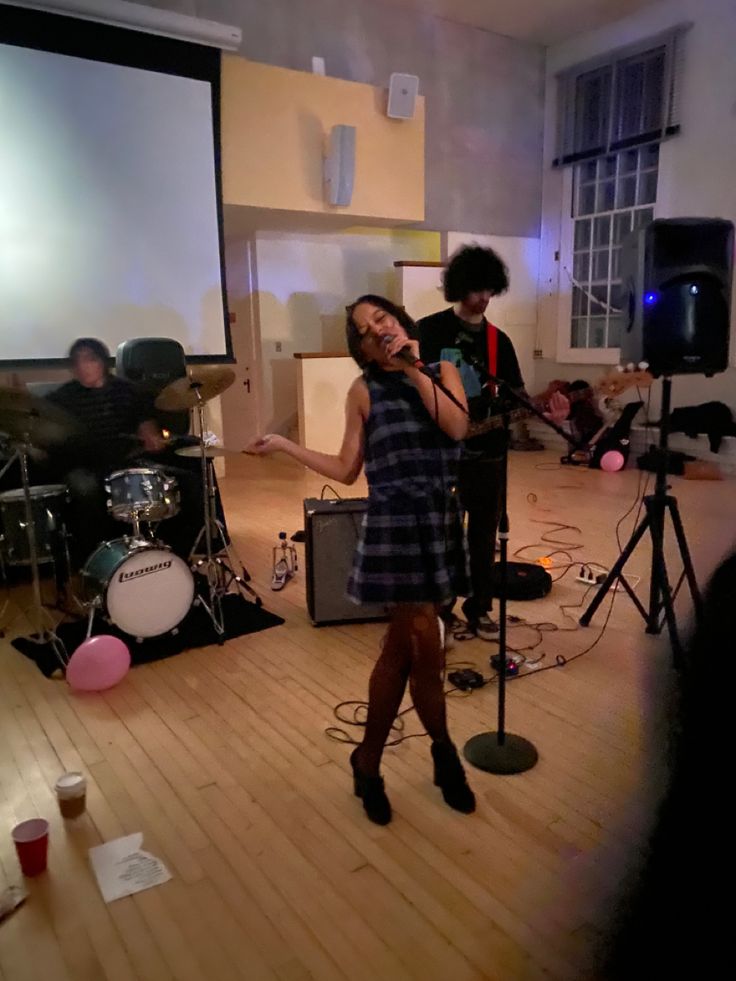 a woman standing in front of a microphone on top of a wooden floor next to other people