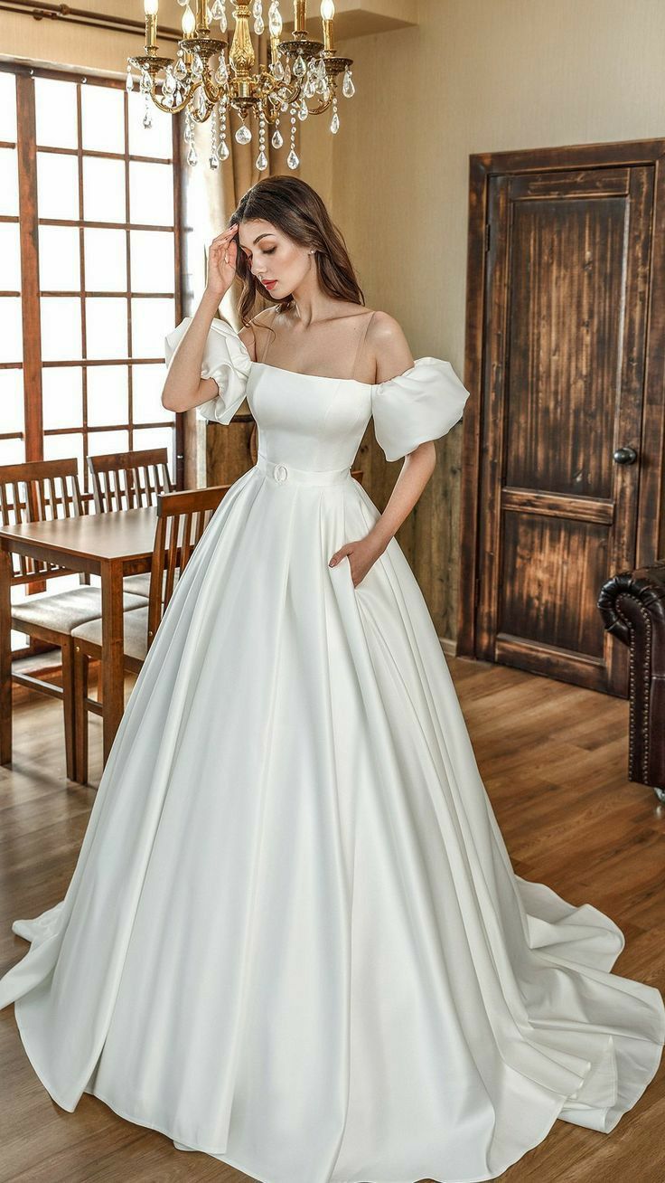 a woman in a white wedding dress standing on a wooden floor next to a table