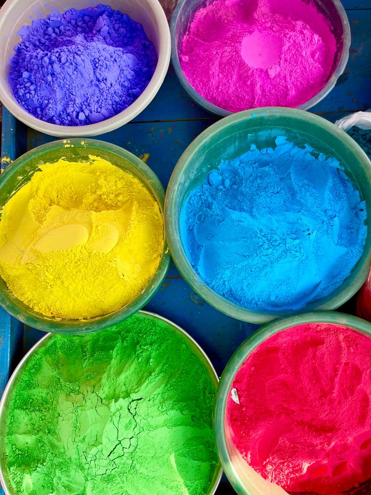 four bowls filled with colored powder on top of a blue tray