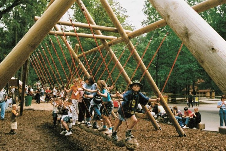 several children are playing on a wooden structure in the park while adults watch from behind