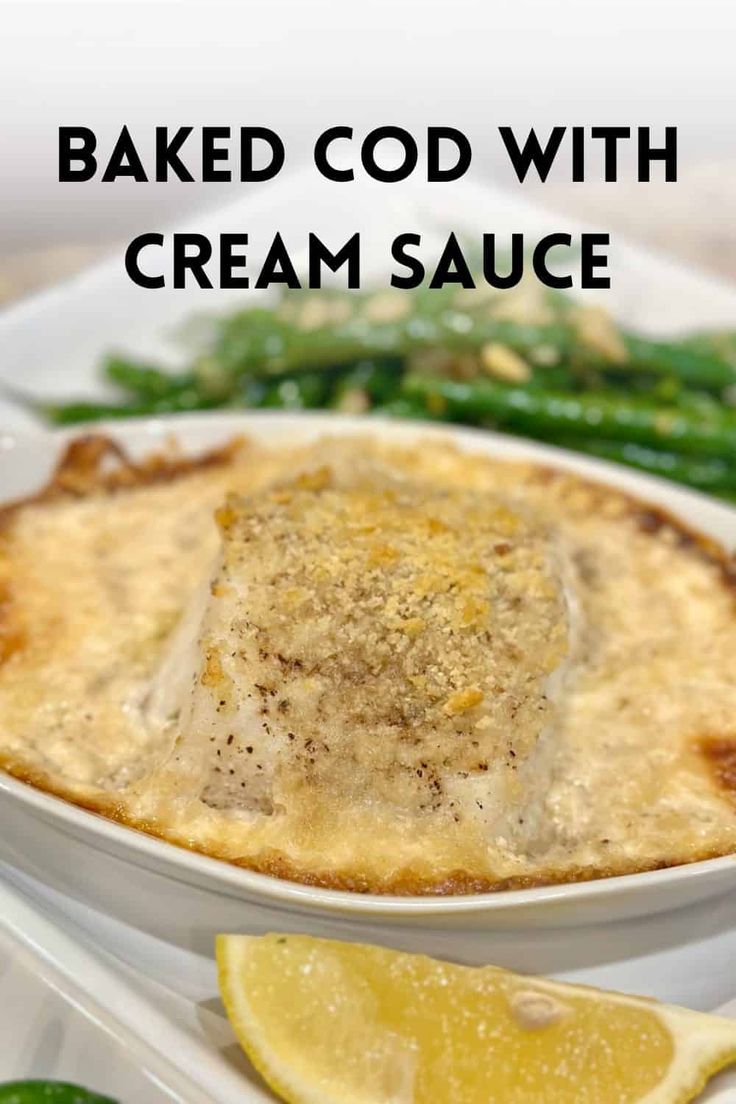 baked cob with cream sauce in a white bowl next to green beans and lemon wedges