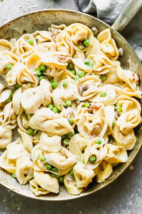 a skillet filled with pasta and peas on top of a gray table next to a fork