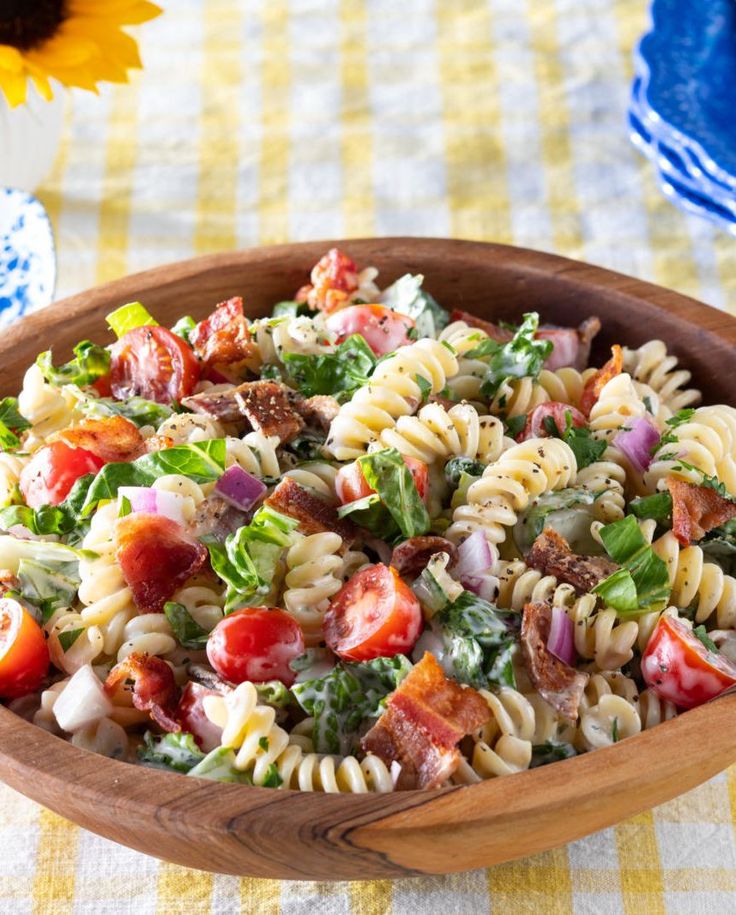 a wooden bowl filled with pasta salad next to a yellow and white checkered table cloth