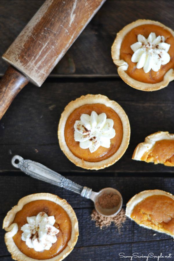 pumpkin pies with whipped cream on top sitting on a wooden table next to a knife