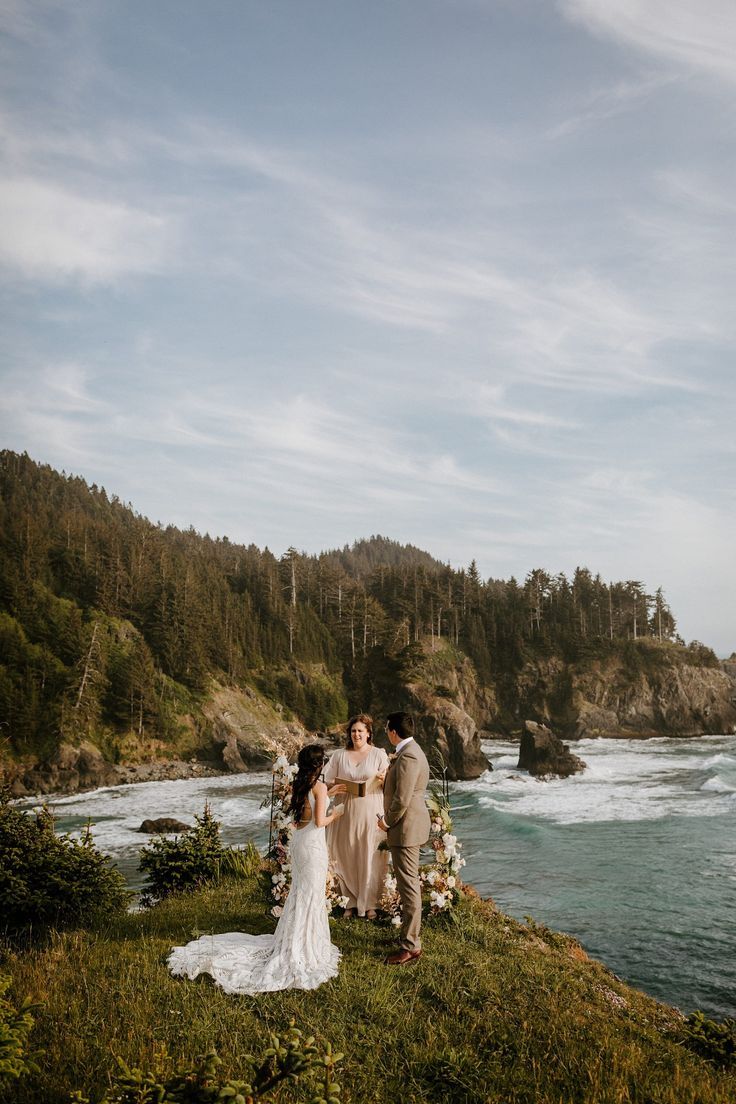 a bride and groom standing on top of a hill next to the ocean