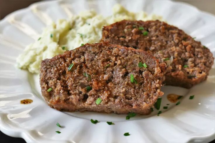 two meat patties on a paper plate with mashed potatoes