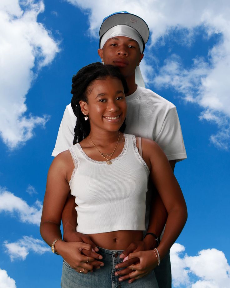 a man and woman are standing in front of a blue sky with white fluffy clouds