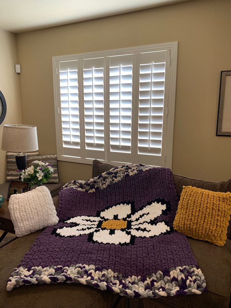 a living room with a couch covered in a crochet kitty blanket and pillows