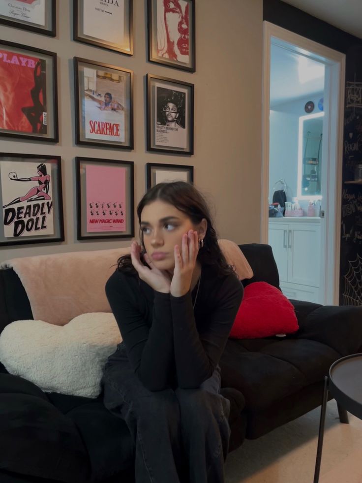 a woman sitting on top of a couch next to a wall with pictures above her