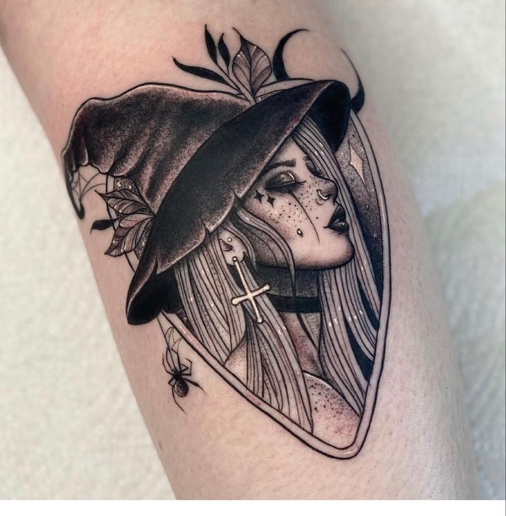 a woman's leg with a black and white tattoo design on it, featuring a witch