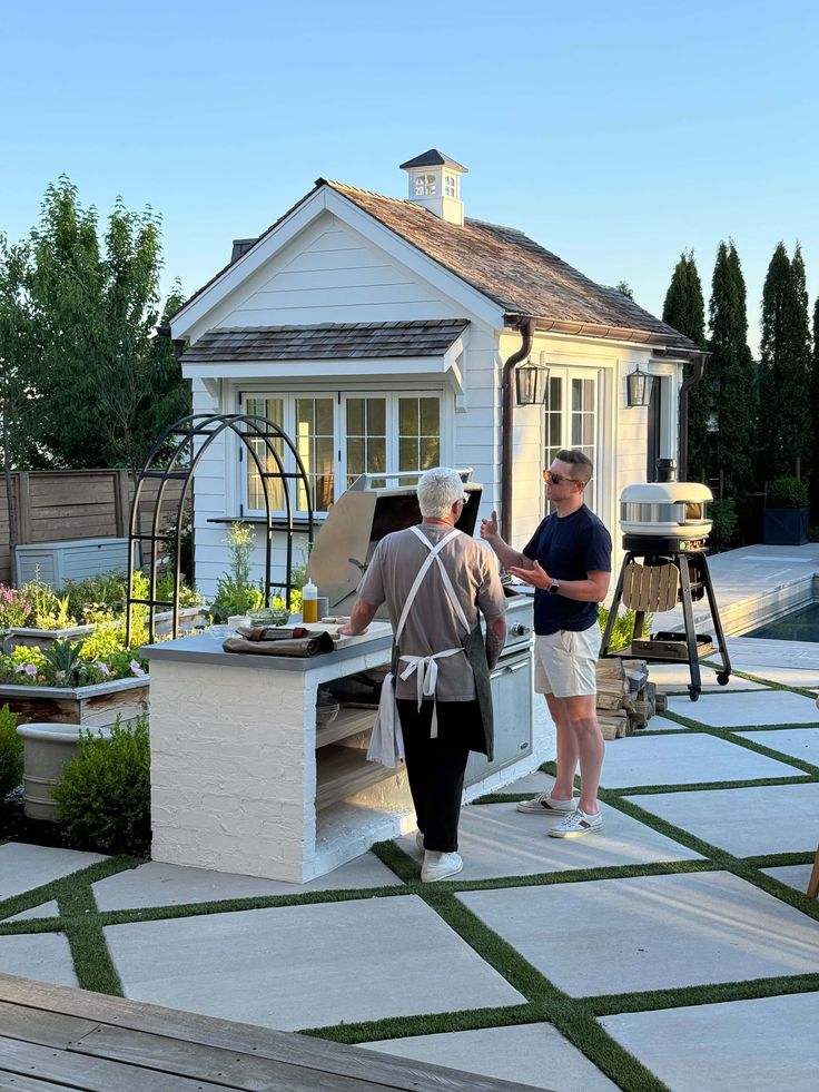 two people are standing in the back yard with an outdoor kitchen and bbq grill