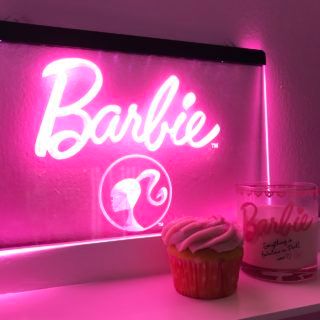 a cupcake sitting on top of a counter next to a pink neon sign that says barbie