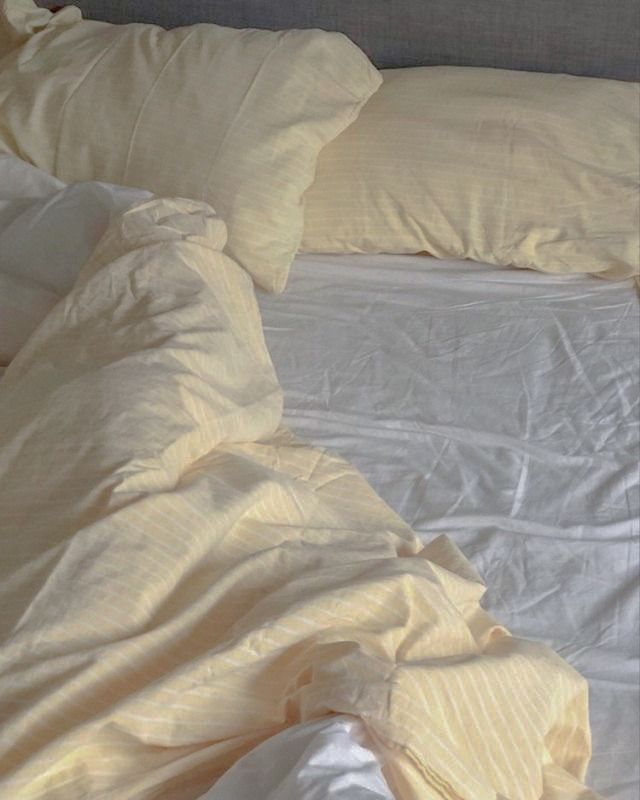 an unmade bed with white sheets and yellow pillows