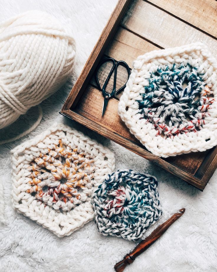 three crocheted coasters in a wooden box with yarn and scissors on the floor