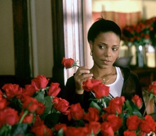 a woman holding a flower in her hand and looking at the flowers on the table