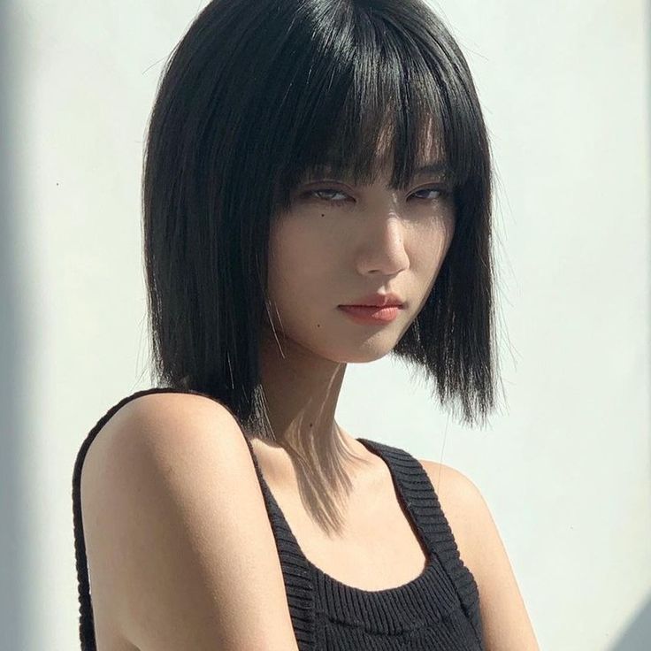 a woman with black hair and bangs standing in front of a white wall looking at the camera