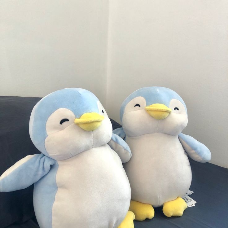 two stuffed penguins sitting next to each other on a black couch with white walls in the background