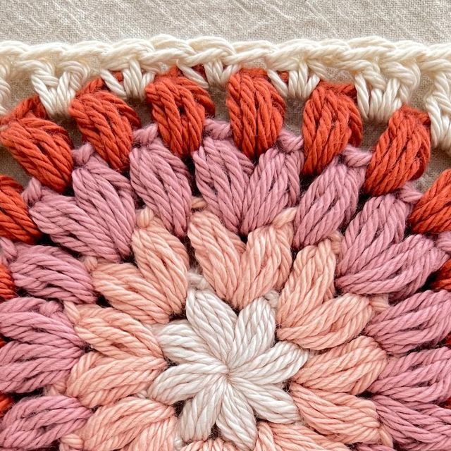 a crocheted square with an orange, pink and white flower on the center