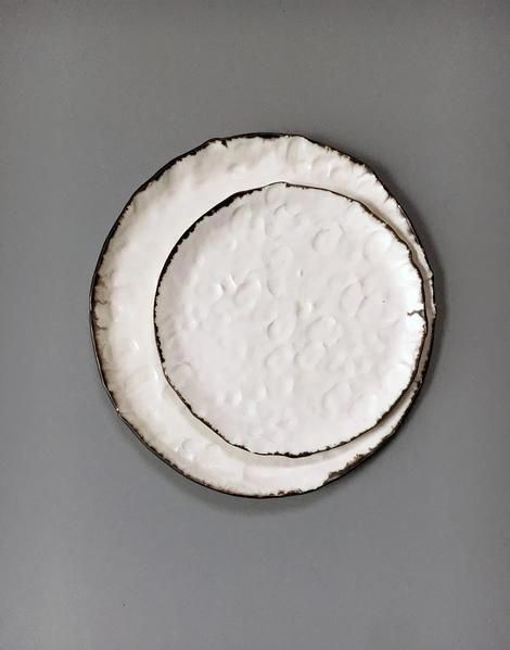 two white plates sitting side by side on a gray tableclothed surface, one is empty