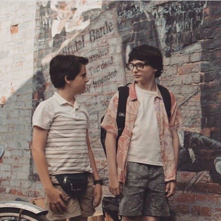 two young boys standing next to each other in front of a wall with graffiti on it