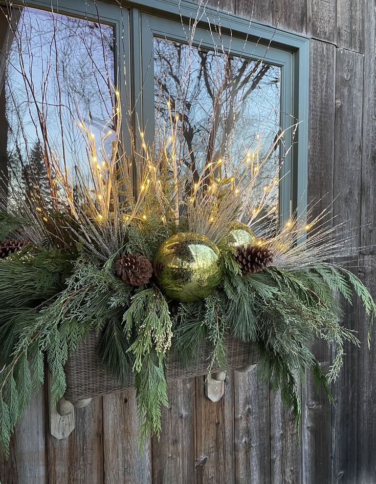 a window sill decorated with evergreen, pine cones and other greenery in front of a wooden building