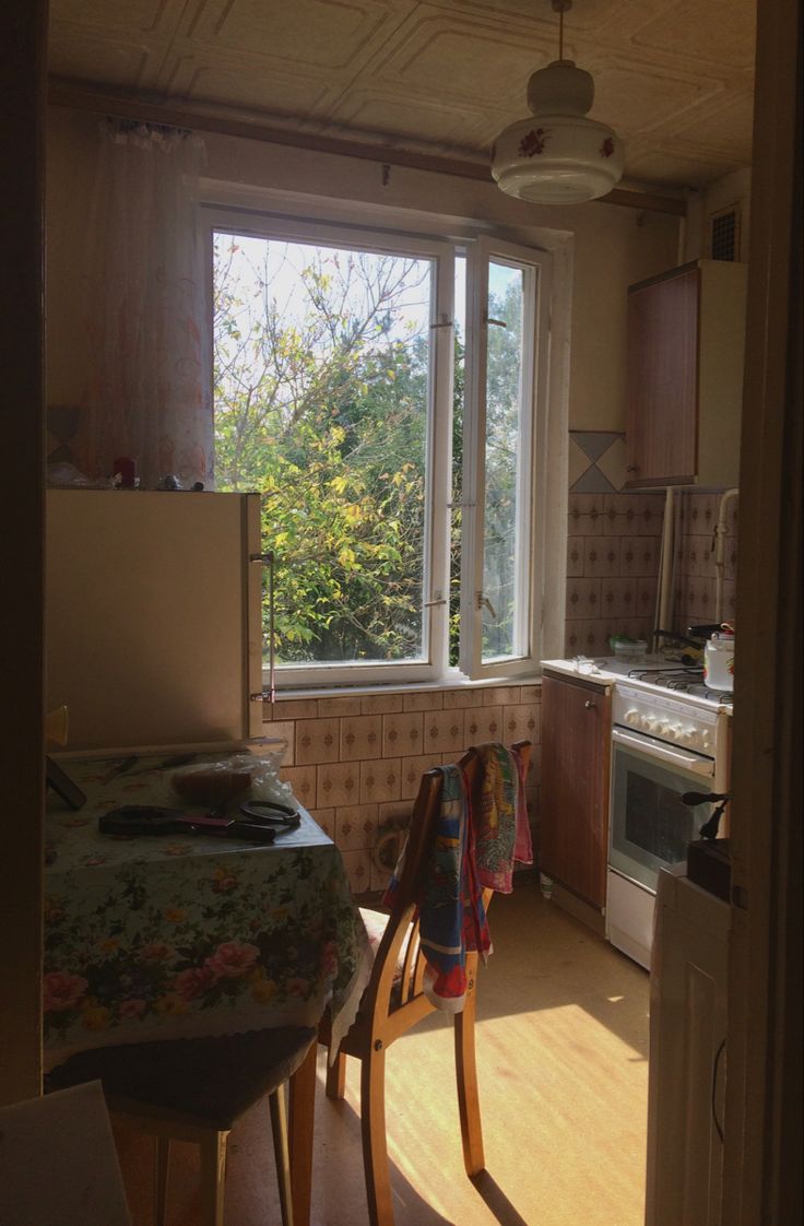 a kitchen with an oven, sink and table next to a window that looks out onto the woods