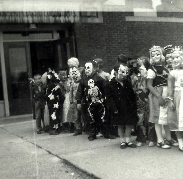 an old black and white photo of children dressed up in halloween costumes standing on the sidewalk