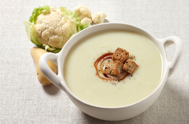 a white bowl filled with soup next to a head of cauliflower