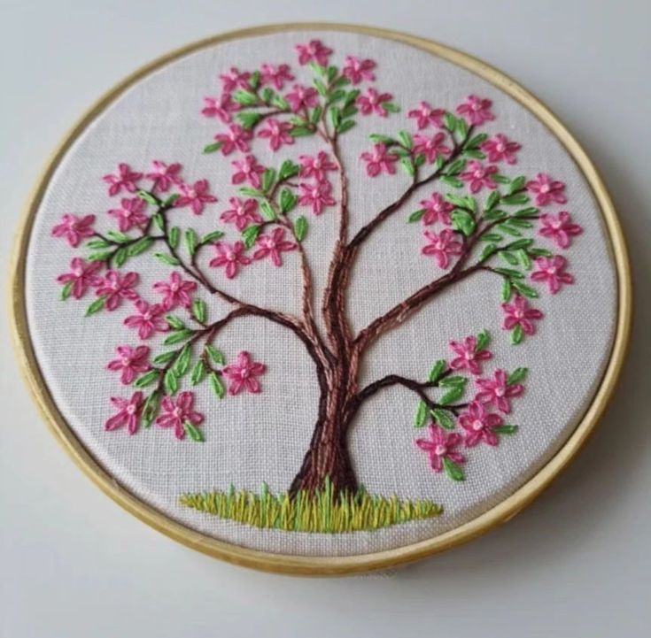 a small embroideryed tree with pink flowers on it's branches and green grass