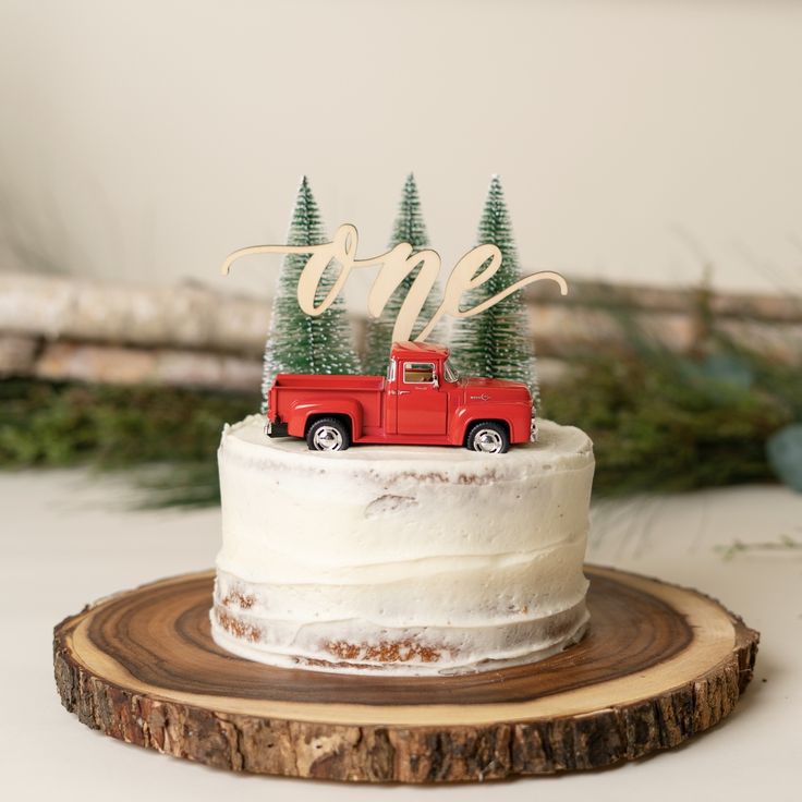 a red truck with trees on top is sitting on a piece of wood next to the cake