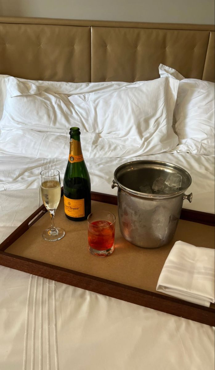 a bottle of wine and two glasses on a tray in front of a bed with white sheets