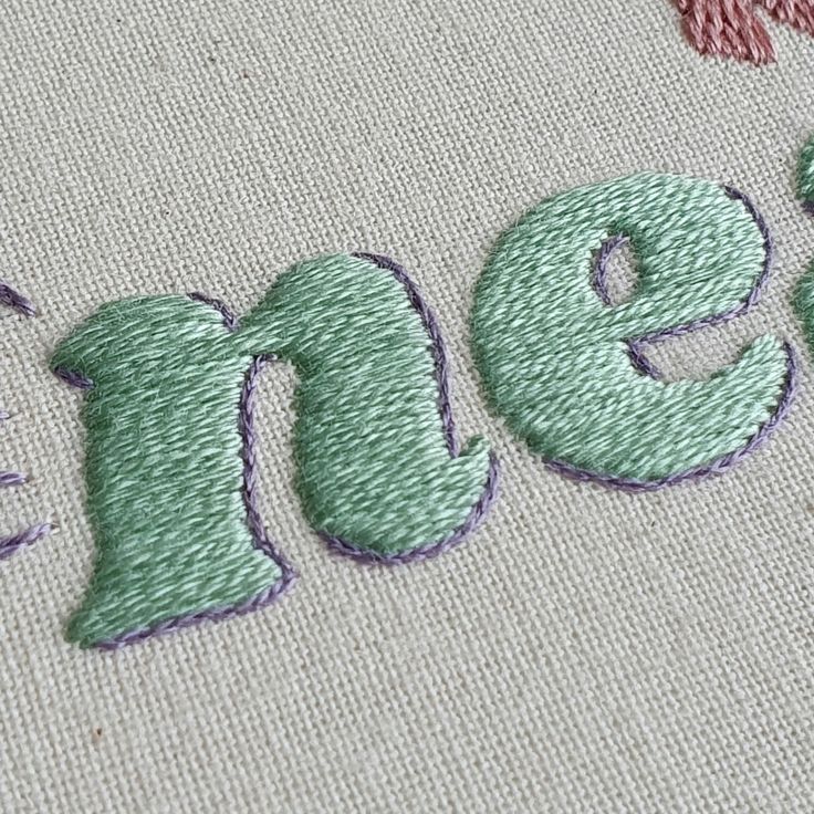 the word stitched on top of a piece of fabric with pink and green thread