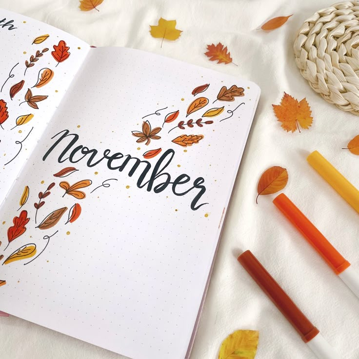 an open notebook with the word november written on it and autumn leaves scattered around it