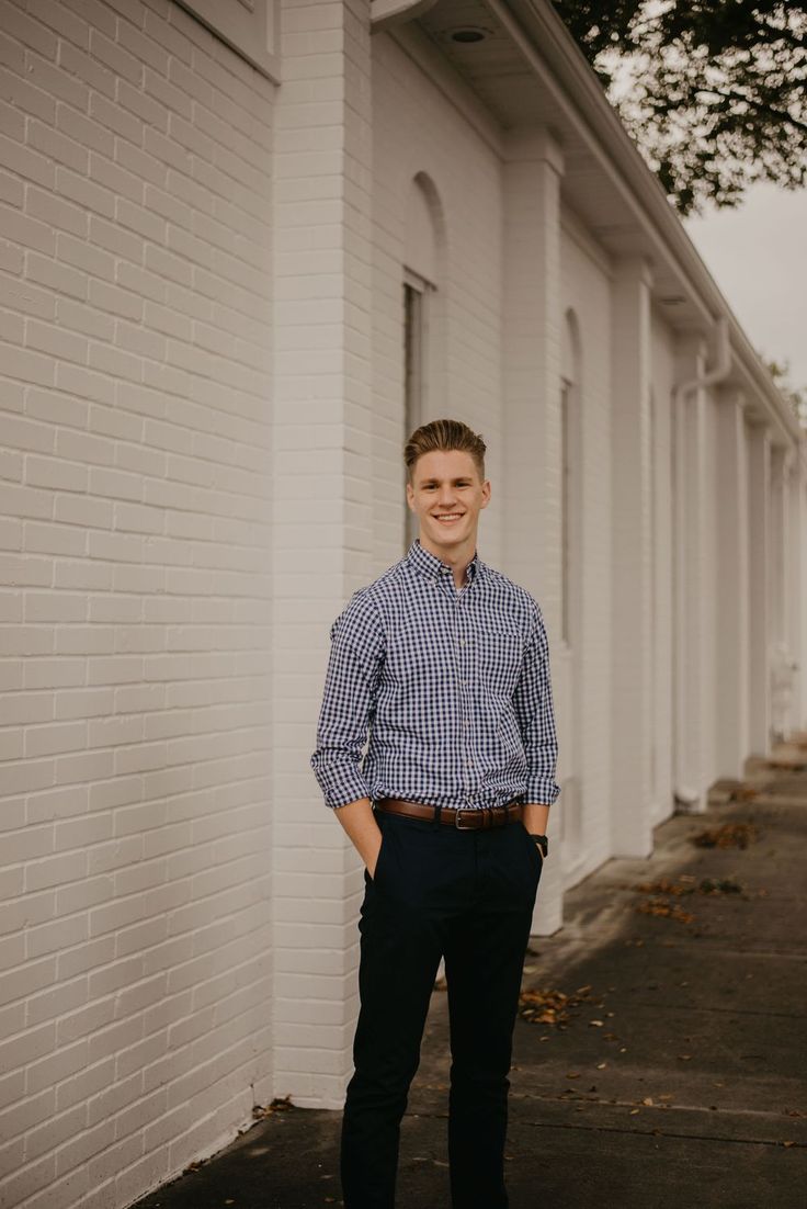 a man standing in front of a white brick building with his hands in his pockets