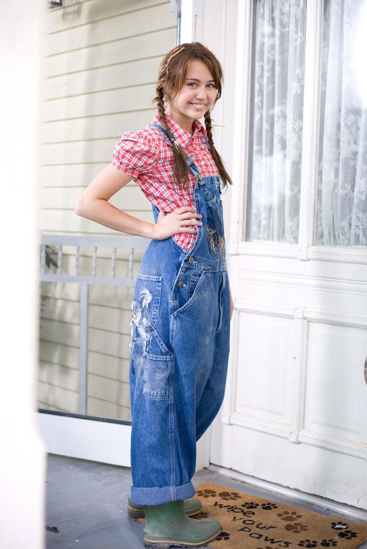 a girl in overalls standing on the front porch