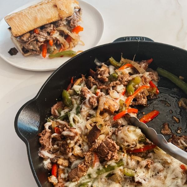 a pan filled with meat and veggies next to a sandwich on a plate