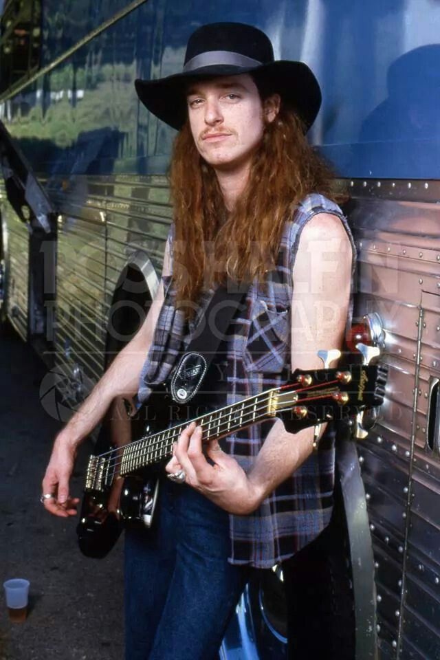 a man with long red hair wearing a cowboy hat and playing an electric guitar in front of a bus