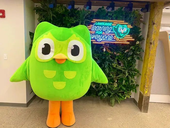 a green bird mascot standing in front of a sign