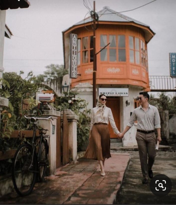 a man and woman holding hands while walking down the street in front of an orange building