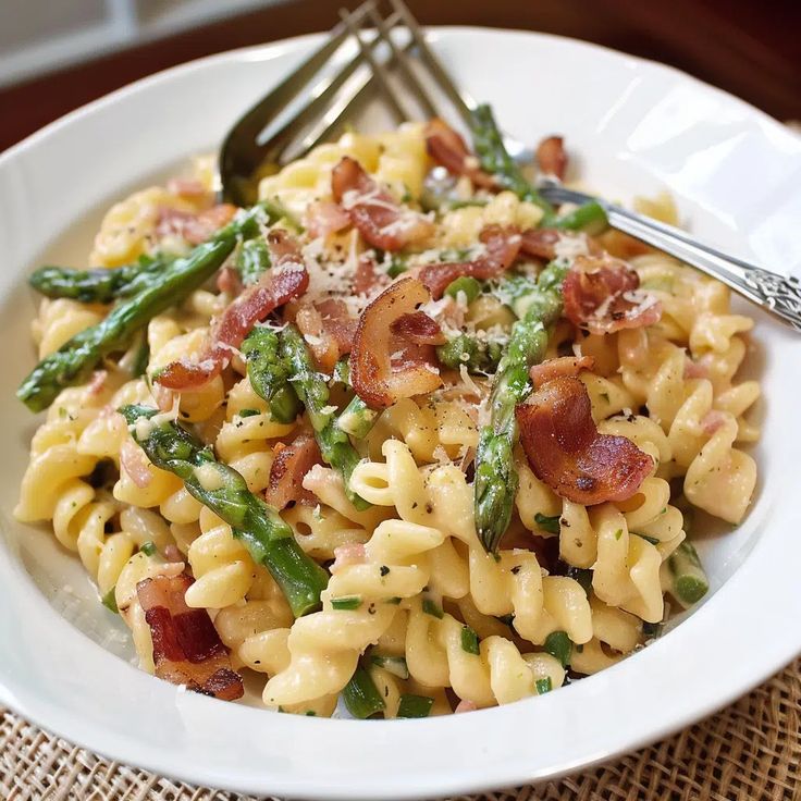 a white bowl filled with pasta and asparagus on top of a wooden table