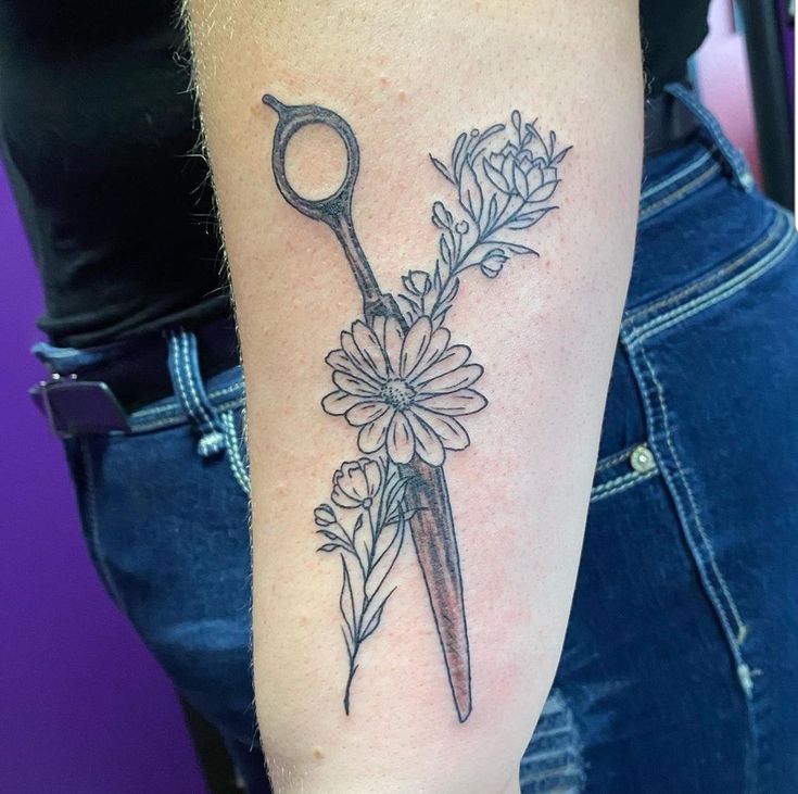 a woman with a tattoo on her arm holding a pair of scissors next to flowers