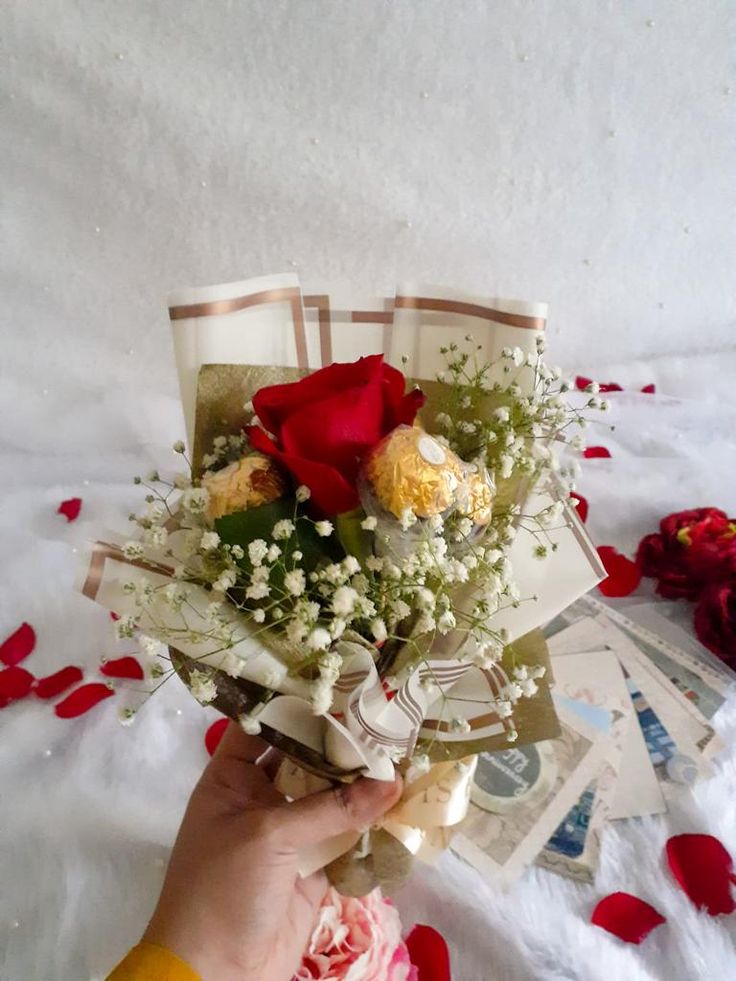 a person holding a bouquet of flowers on top of a white bed covered in red petals