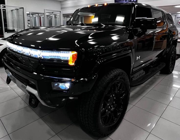 a black truck parked in a showroom with its lights on and the hood up